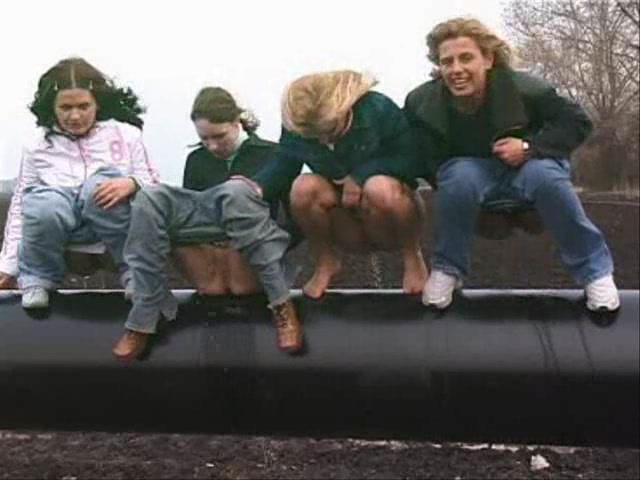 Group of girls pissing outdoors on a pipe