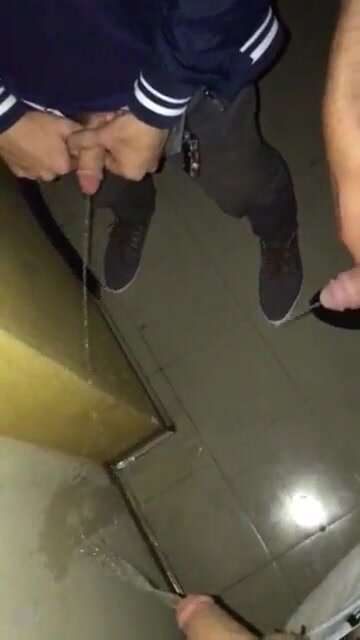 Three friends pissing on wall in building