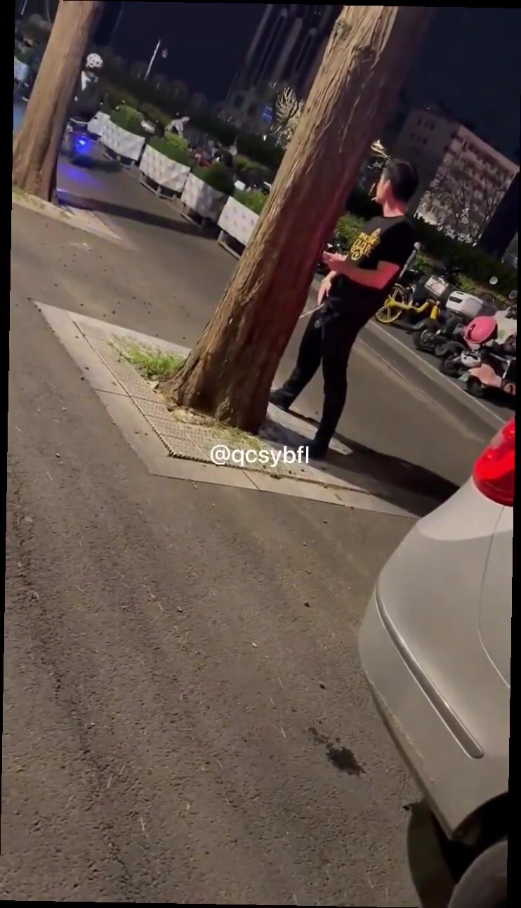 Asian guy pissing on a tree while people pass by