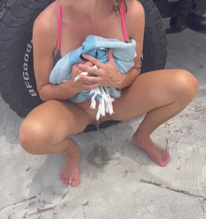 Cutie pees in the sand behind large truck on the beach