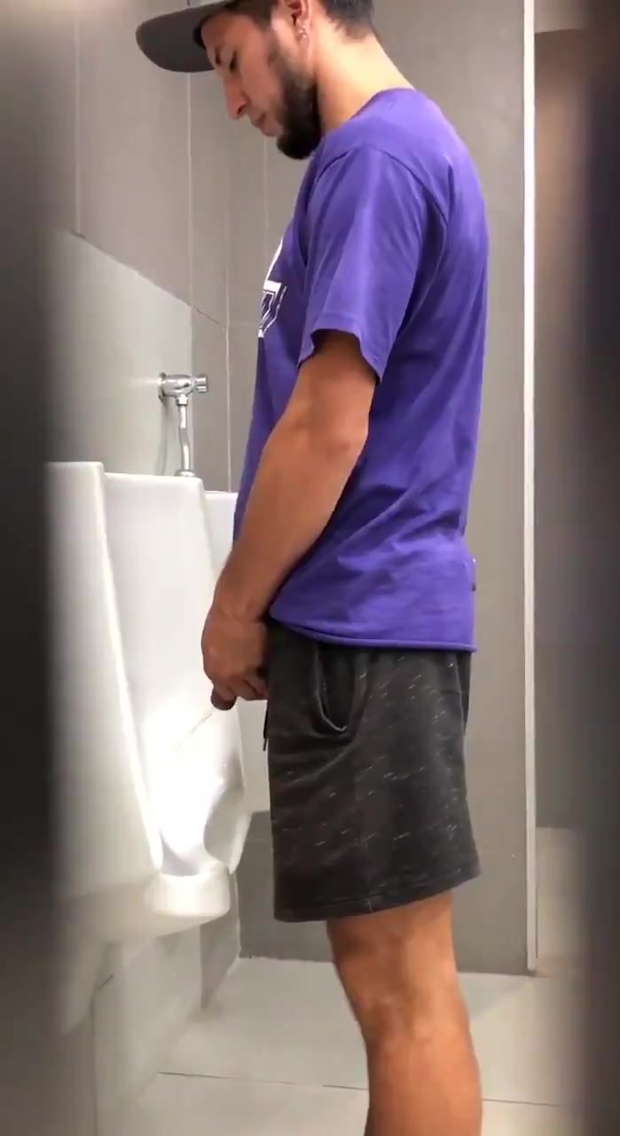 Cap and shorts pissing at the urinal