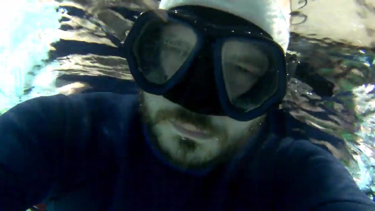 Bald freediver breatholding underwater in wetsuit
