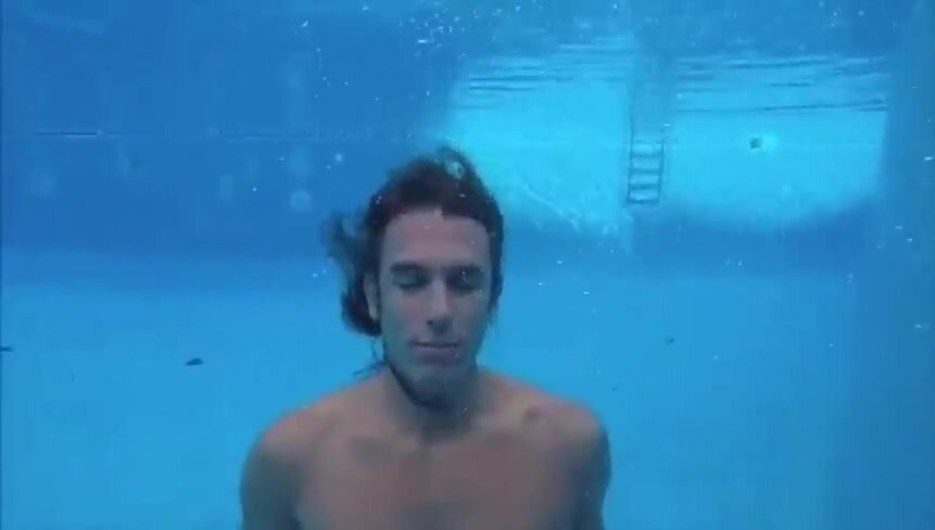 Barefaced clothed guy breatholding underwater