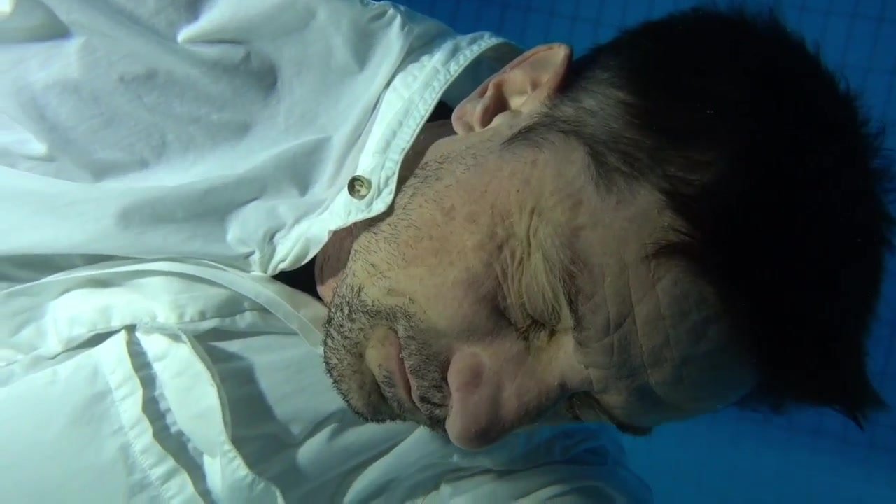 Clothed barefaced man sinking underwater