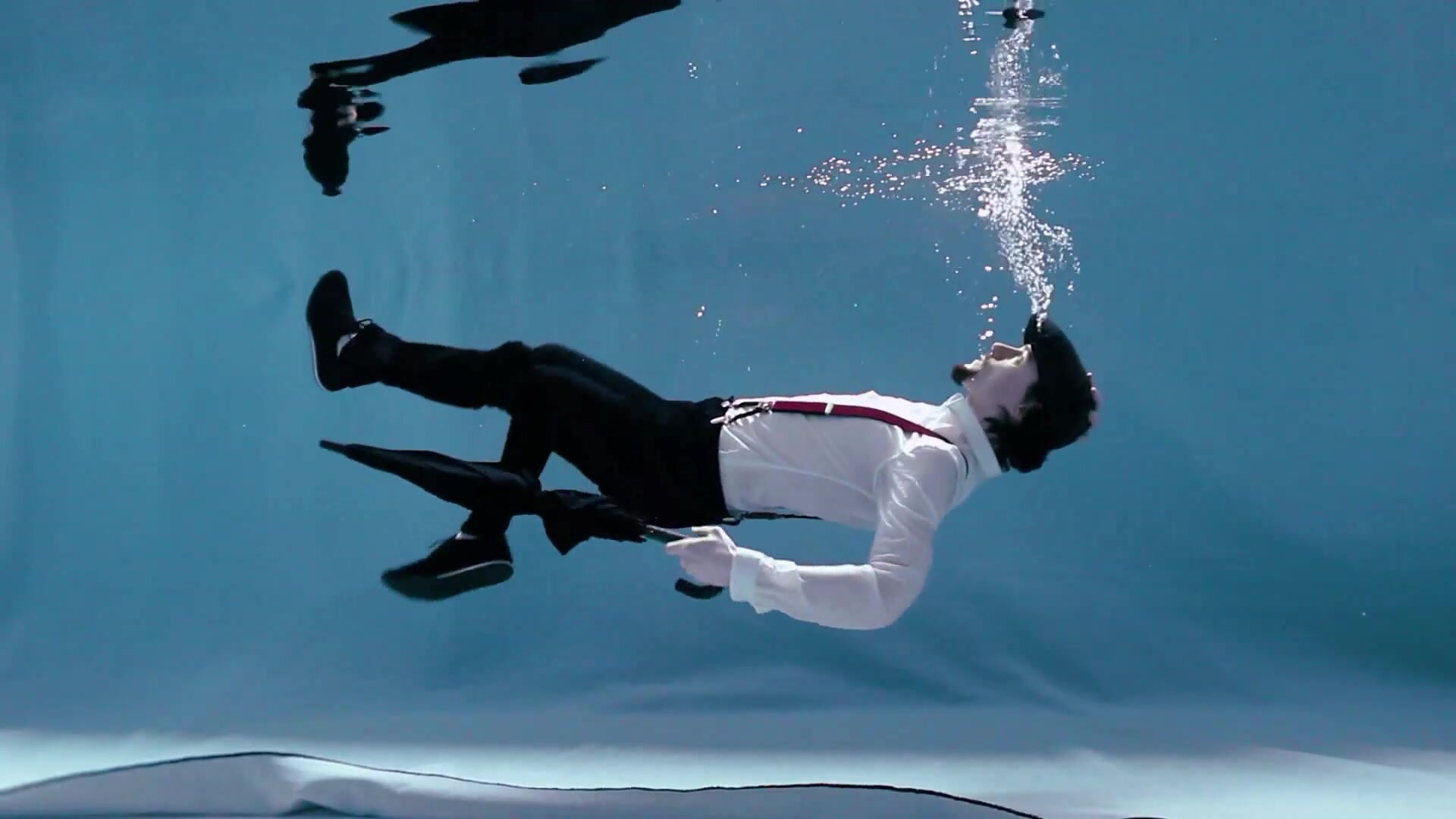 Clothed barefaced guy underwater in pool