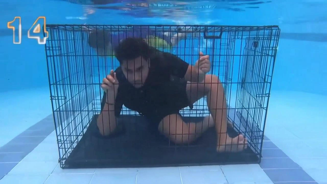 Clothed barefaced guy underwater in cage