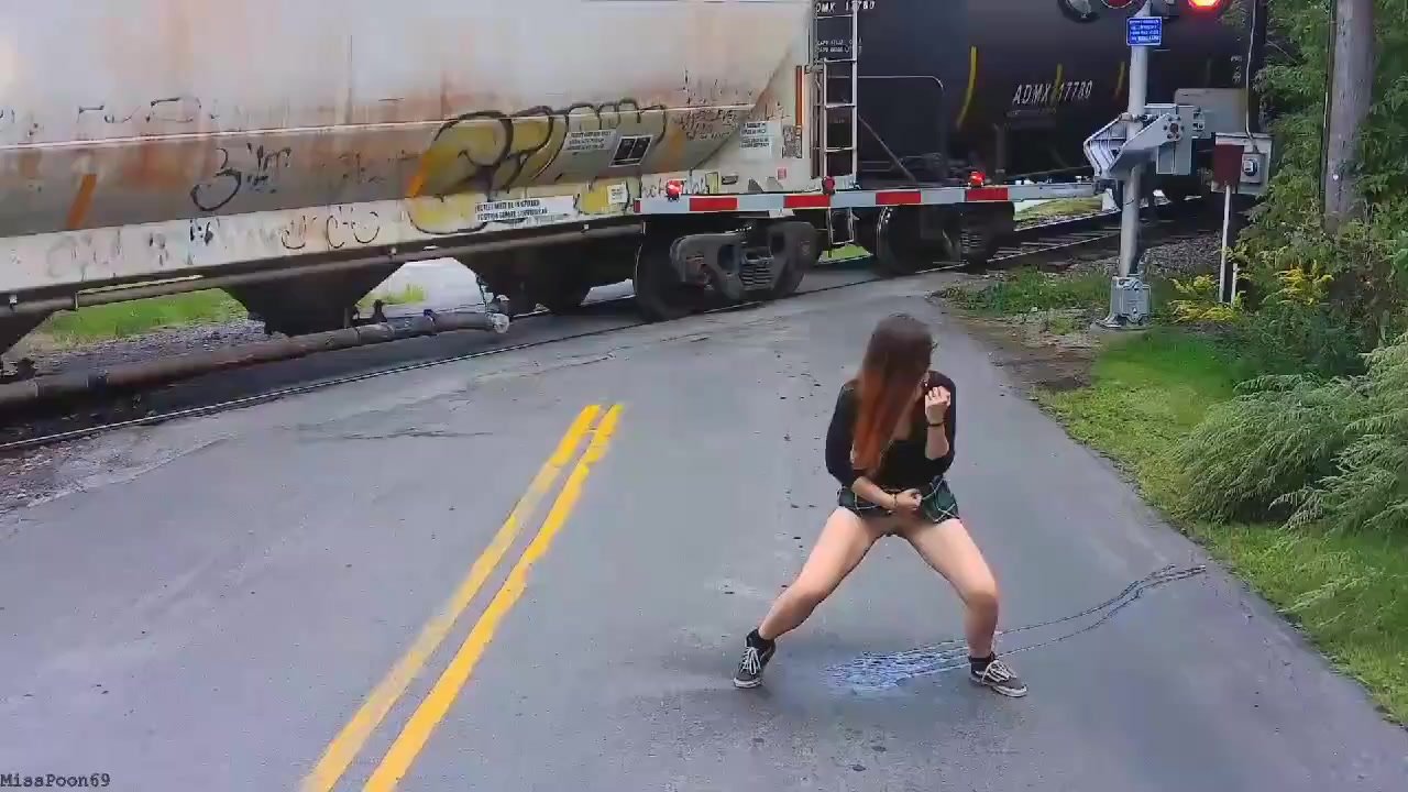 Girl pees on the street in front of a passing train