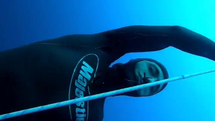 Barefaced underwater freediver in tight wetsuit