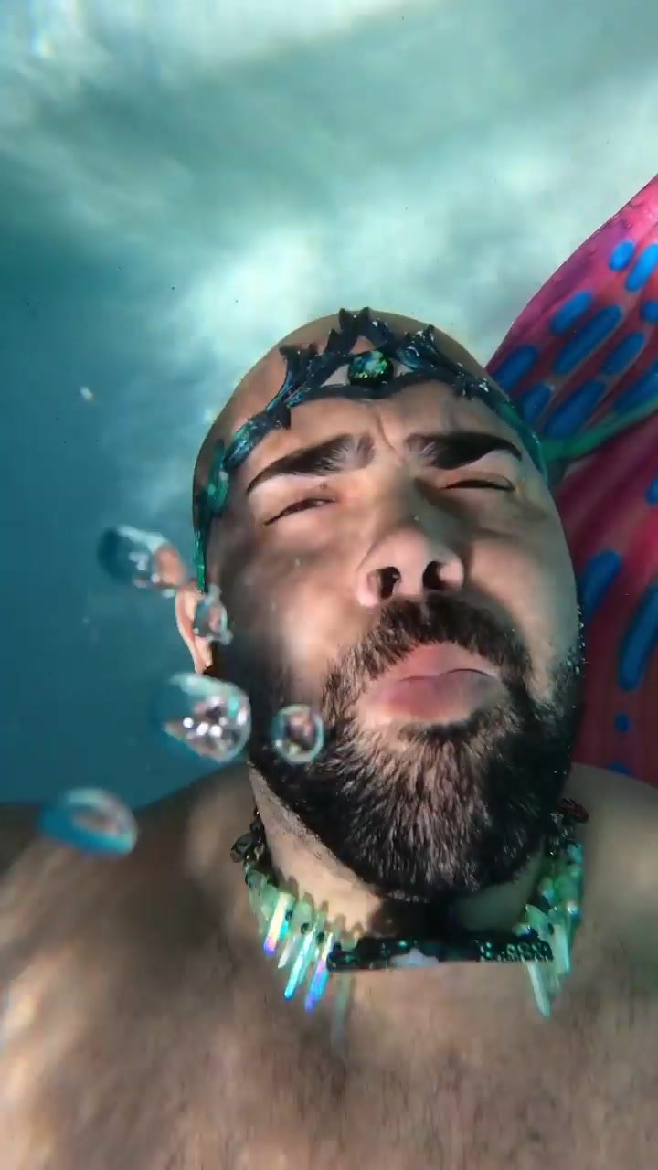 Bald merman blowing bubbles barefaced underwater