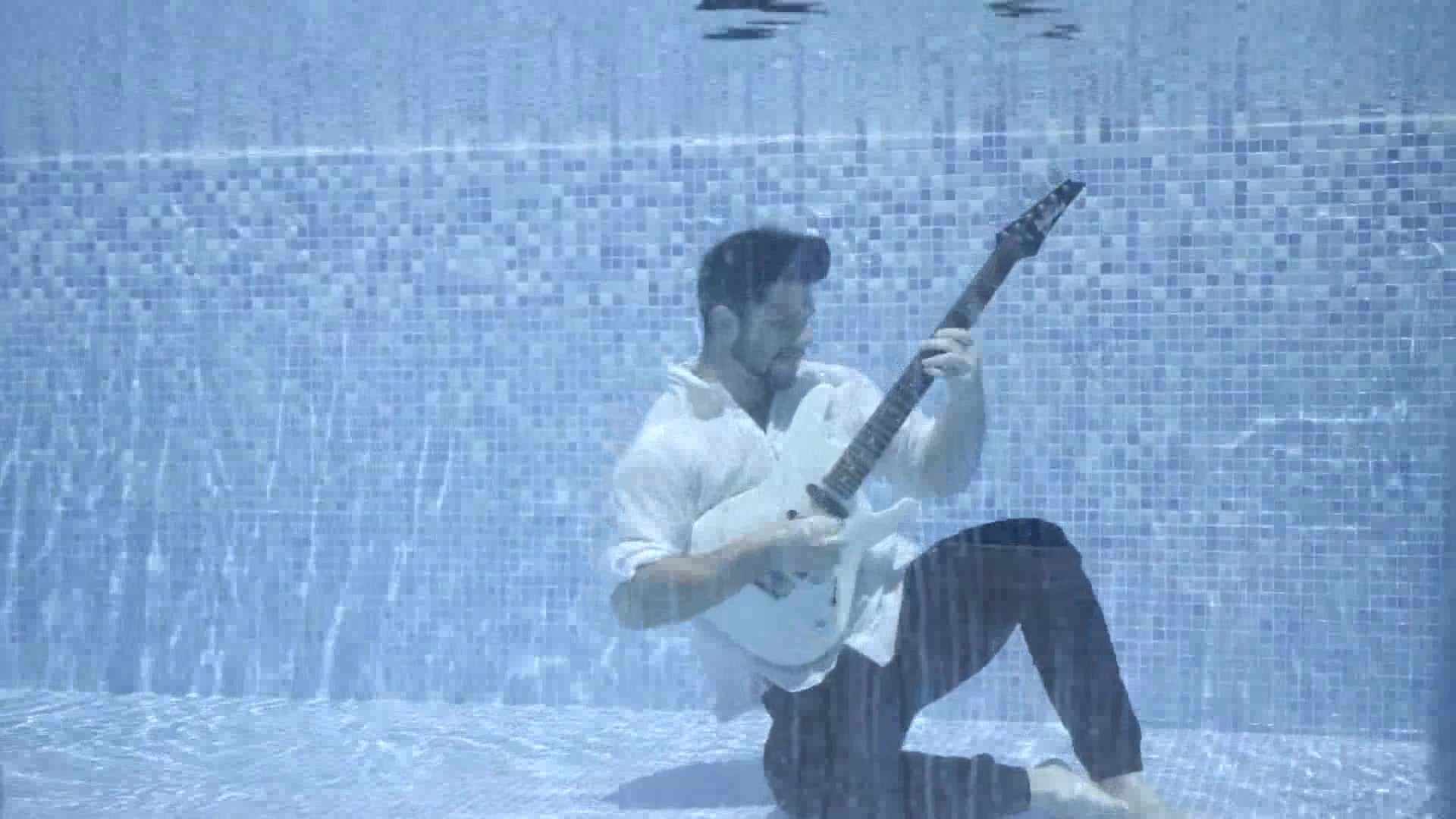 Clothed barefaced bearded guy singing underwater