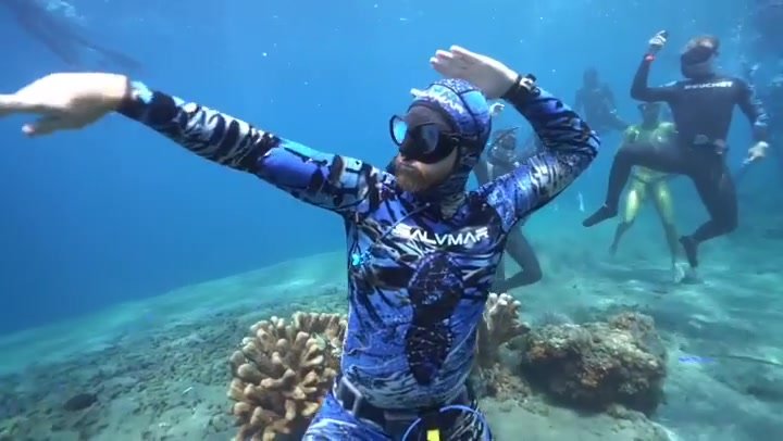 Wetsuit freedivers dancing underwater