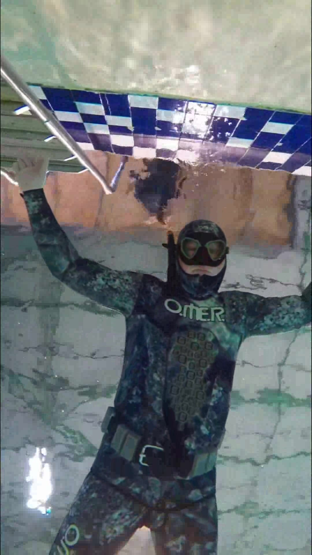 Underwater beefy freediver in tight wetsuit