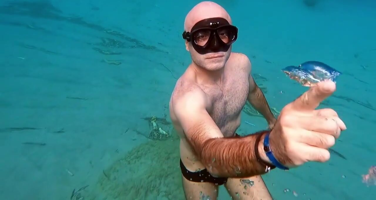 Bald freediver breatholds underwater in speedo