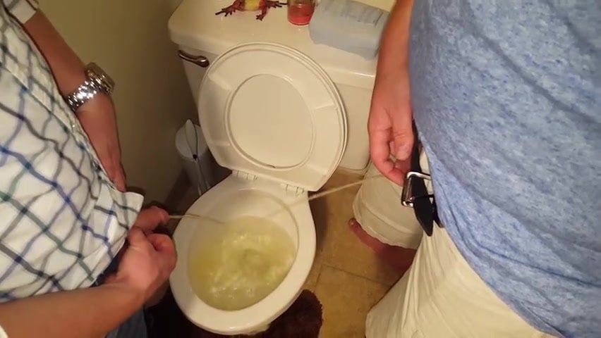 Two guys pee piss in a toilet
