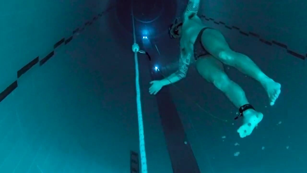 Tattooed speedo freediver diving deep underwater