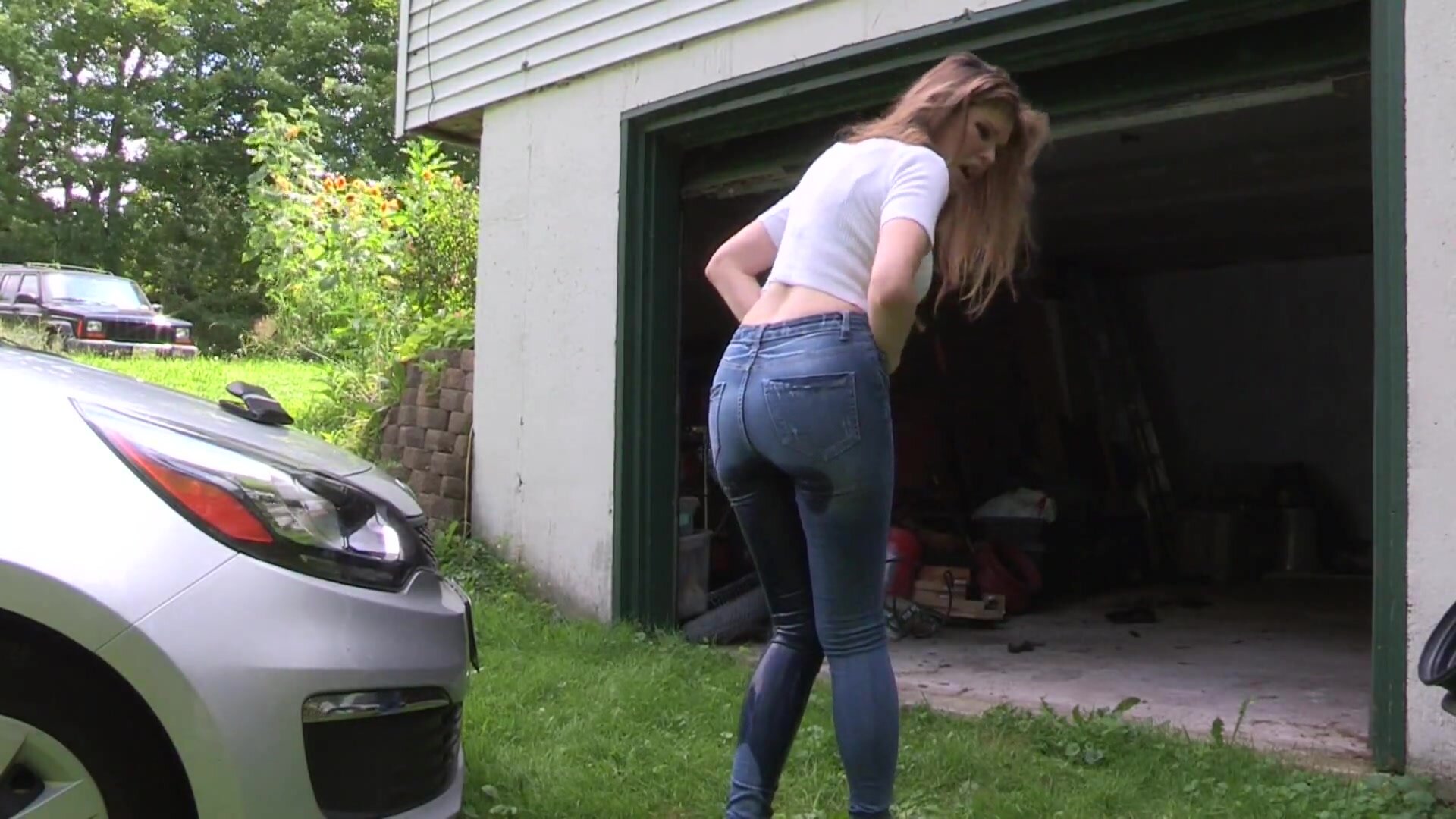 blonde gir pees in jeans in front of a garage  ( Clip )