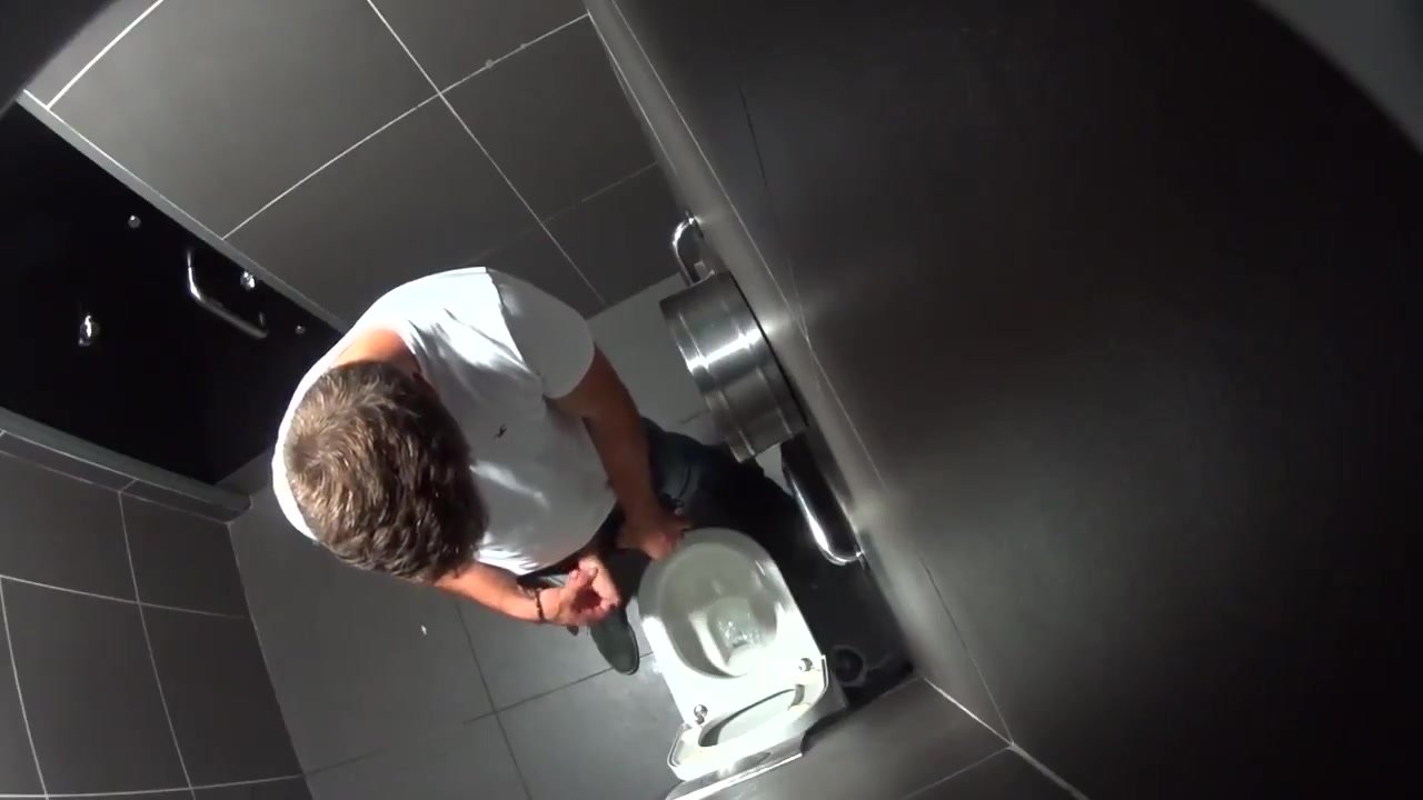 Guy in a white T-shirt peeing in the stall