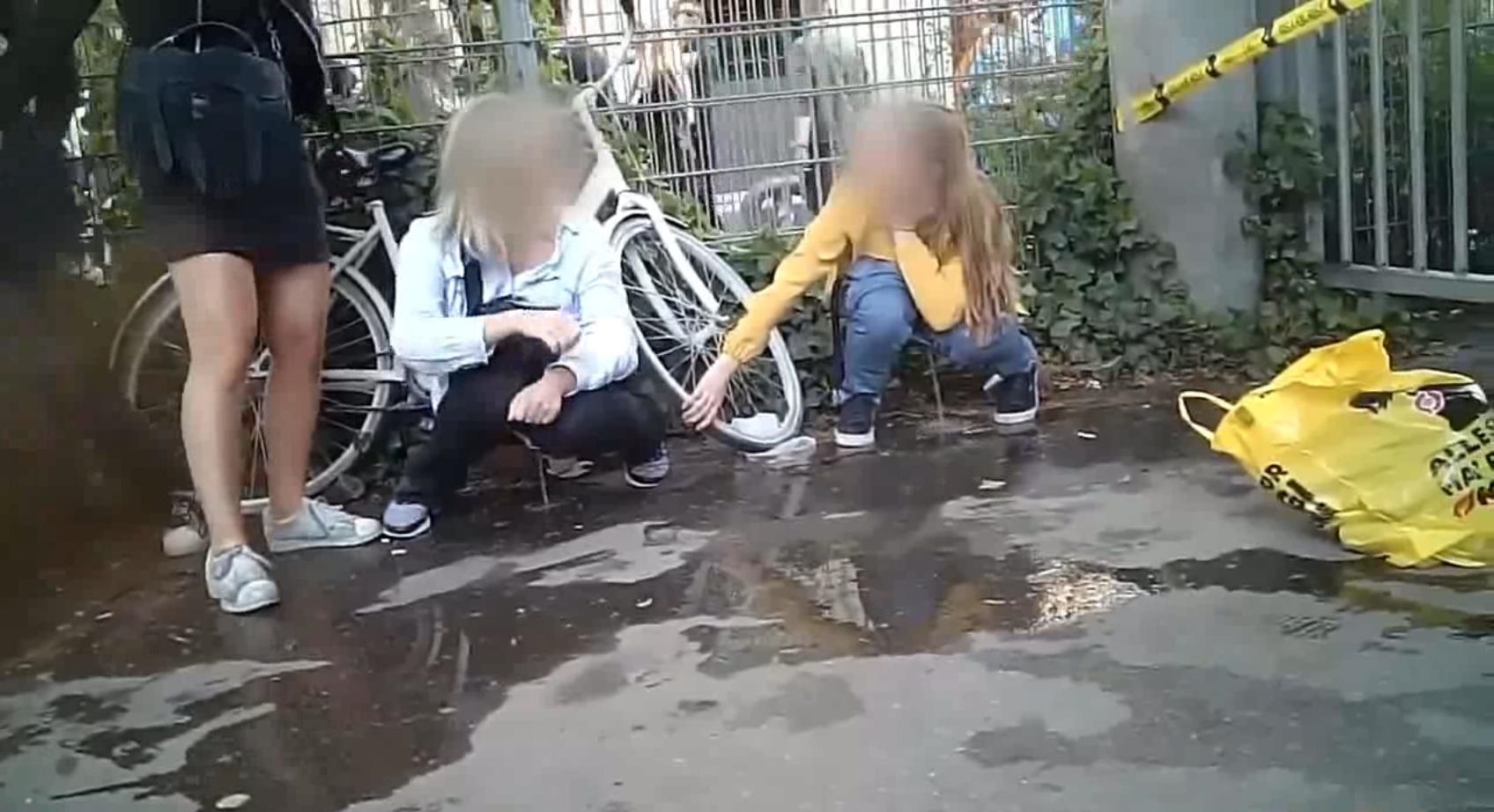 Two girls squat and piss on the asphalt