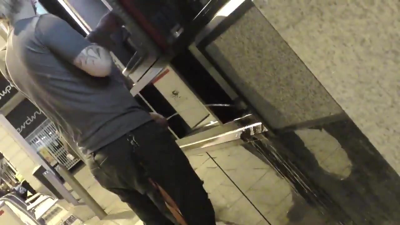 Guy pissing while using cash machine next to a friend