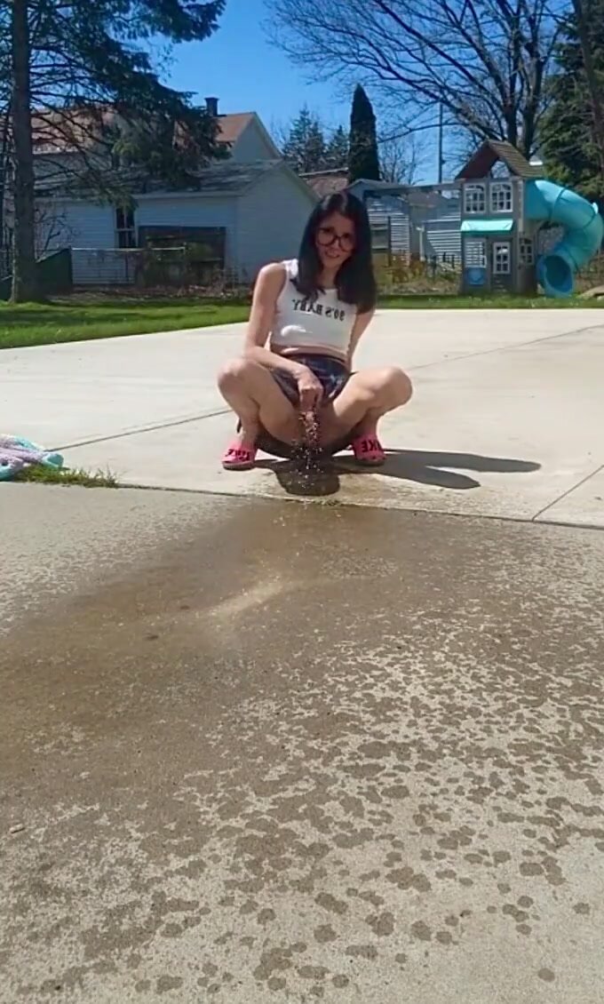 Slim girl sprinkles the pavement in the back yard